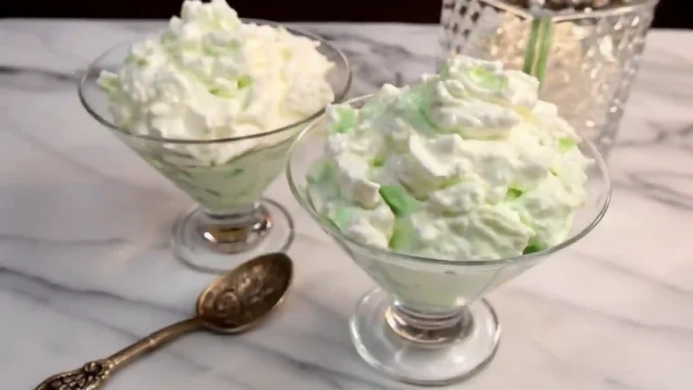 A creamy green pistachio salad served in a glass bowl, garnished with chopped pistachios and maraschino cherries, showcasing its fluffy texture and retro charm