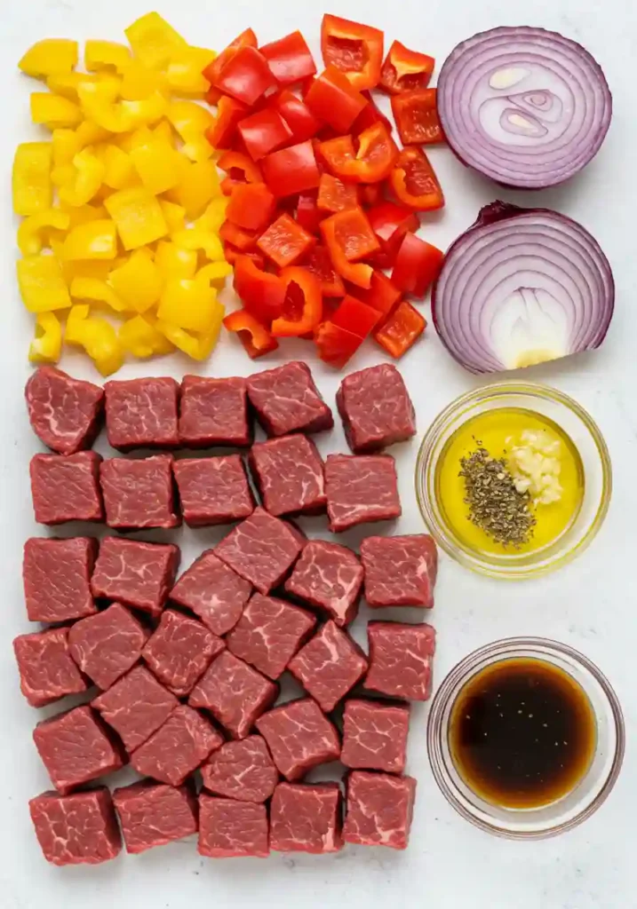 Raw steak cubes, vegetables, marinade ingredients, and skewers for steak kabobs on the grill