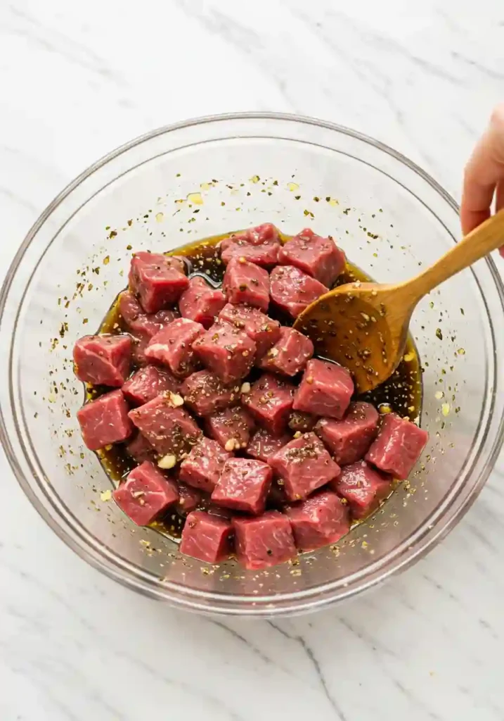 Steak cubes coated in marinade with soy sauce, garlic, and herbs in a bowl