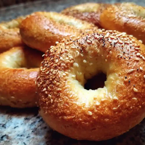 How to Make Perfect Sourdough Discard Bagels at Home Freshly baked sourdough discard bagels on a wooden board with cream cheese.