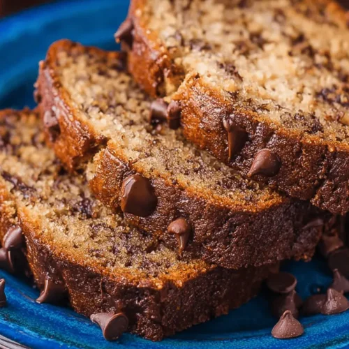 The Ultimate Chocolate Chip Banana Bread Recipe Three moist slices of homemade chocolate chip banana bread on a blue ceramic plate.