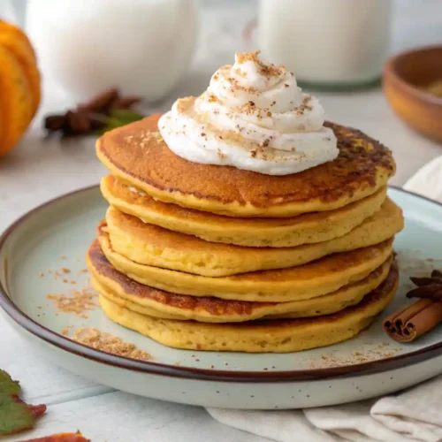 Fluffy pumpkin protein pancakes stacked high with maple syrup drizzle, Greek yogurt topping, and cinnamon on a rustic breakfast table.
