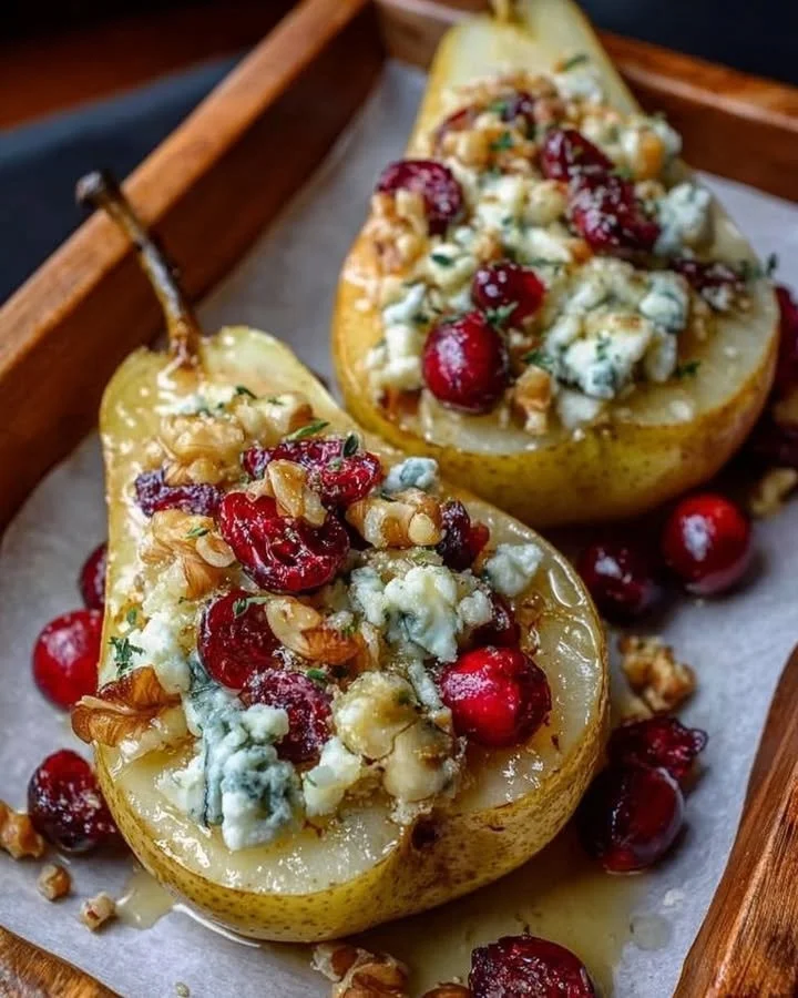 Baked pears topped with cranberries, walnuts, honey, and blue cheese on a plate.