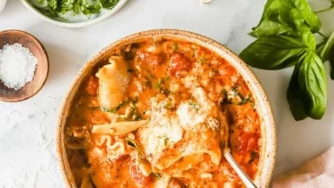 A bowl of easy creamy lasagna soup topped with cheese and herbs, garnished with basil.