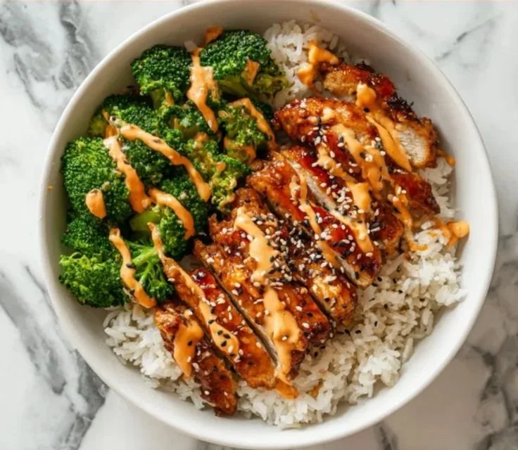 Sticky chicken rice bowl topped with fresh vegetables and sesame seeds