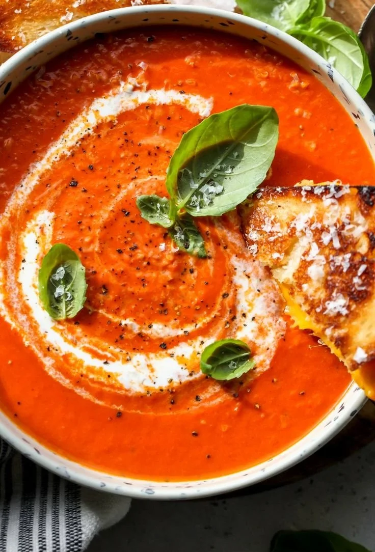 Tomato and Roasted Red Pepper Soup in a bowl with fresh herbs and bread.