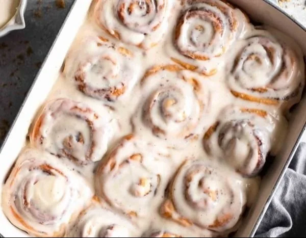 Homemade cinnamon rolls topped with icing on a wooden table