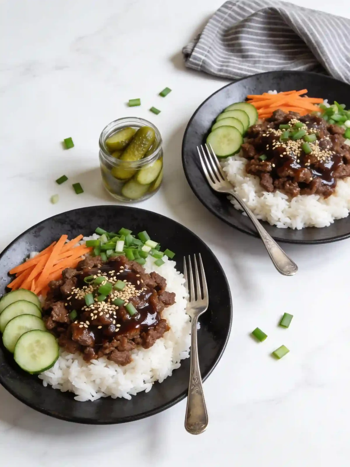Korean Ground Beef Bowl served over white rice with cucumber slices, carrots, green onions, and sesame seeds on a black plate