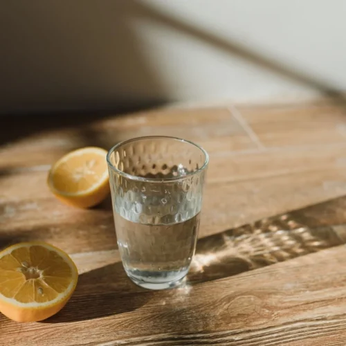 Baking soda recipe for weight loss: a glass of water with lemon halves on a wooden table